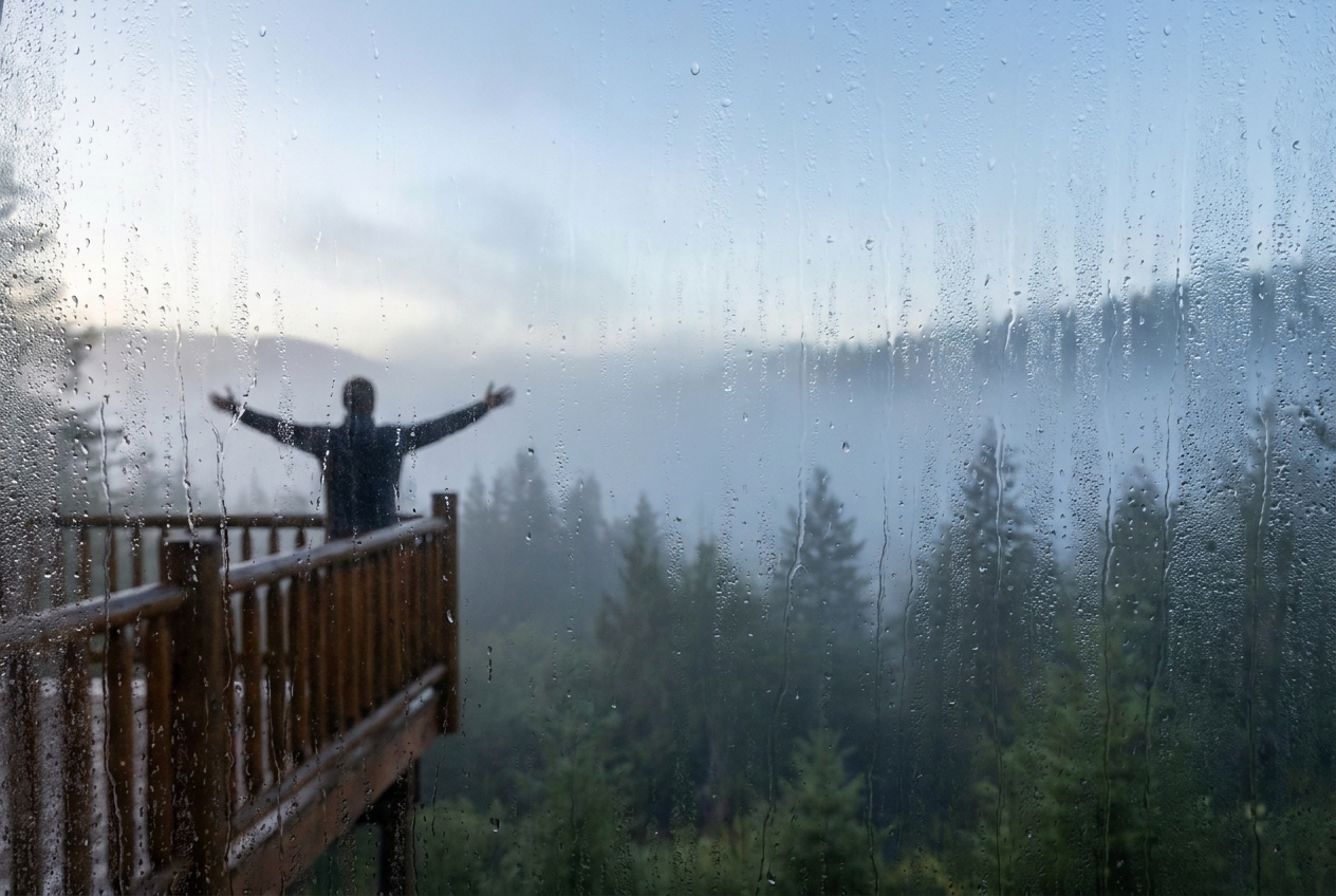 Silhouette of a person stretching on a balcony viewed through a condensation-covered window